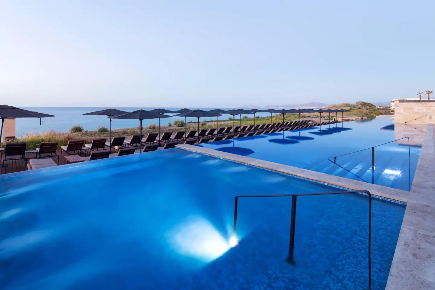Oceanfront infinity pools with umbrellas and loungers at JW Marriott Los Cabos Beach Resort & Spa.