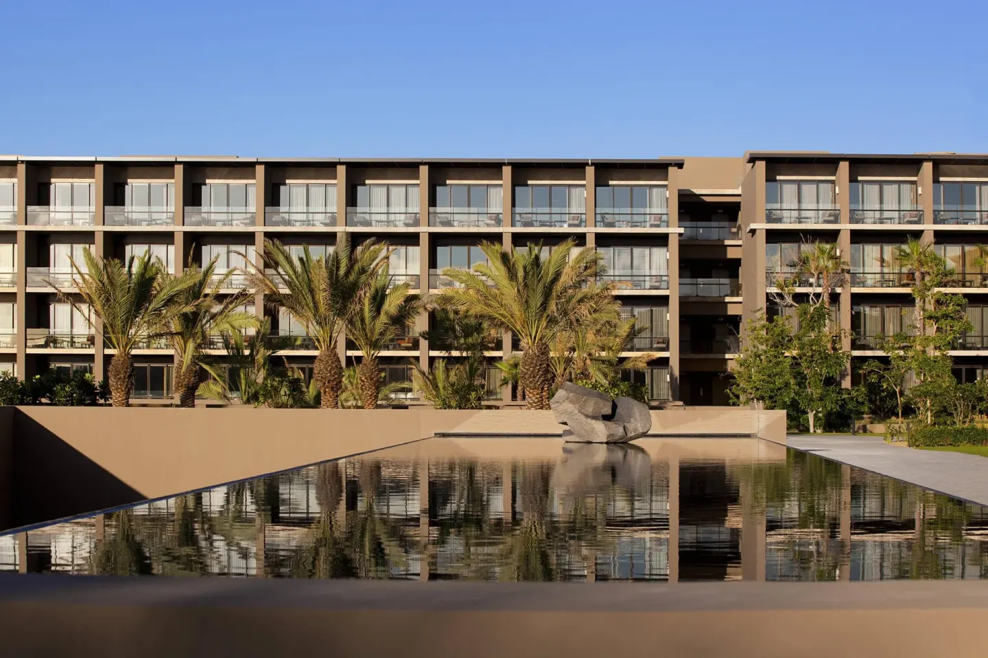 Resort building and palm trees reflected in a pool at JW Marriott Los Cabos Beach Resort & Spa.