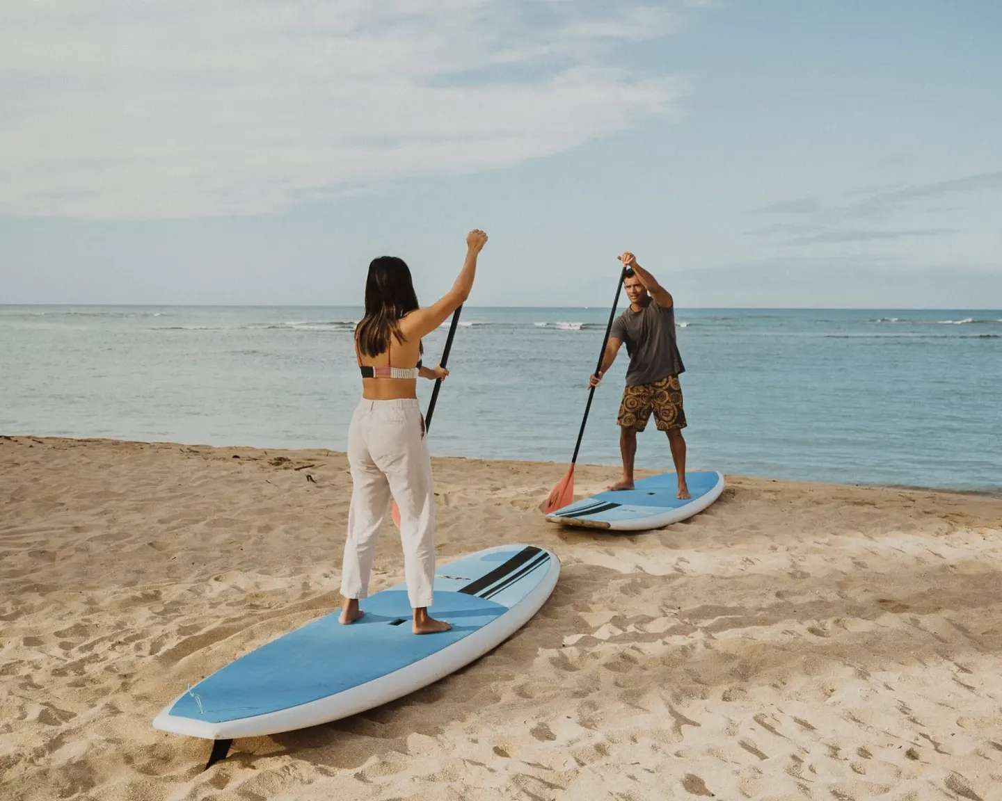 Two people standing on paddleboards on the beach at Kaimana Beach Hotel.