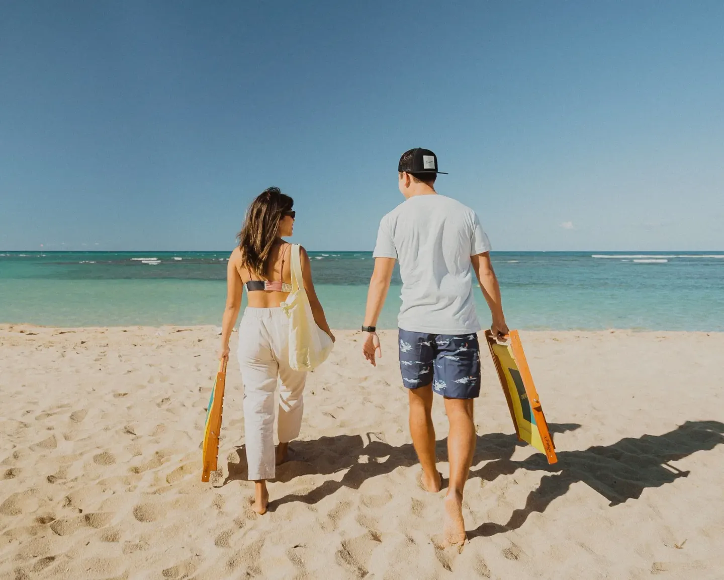 Two guests walk across the sand toward the ocean at Kaimana Beach Hotel.