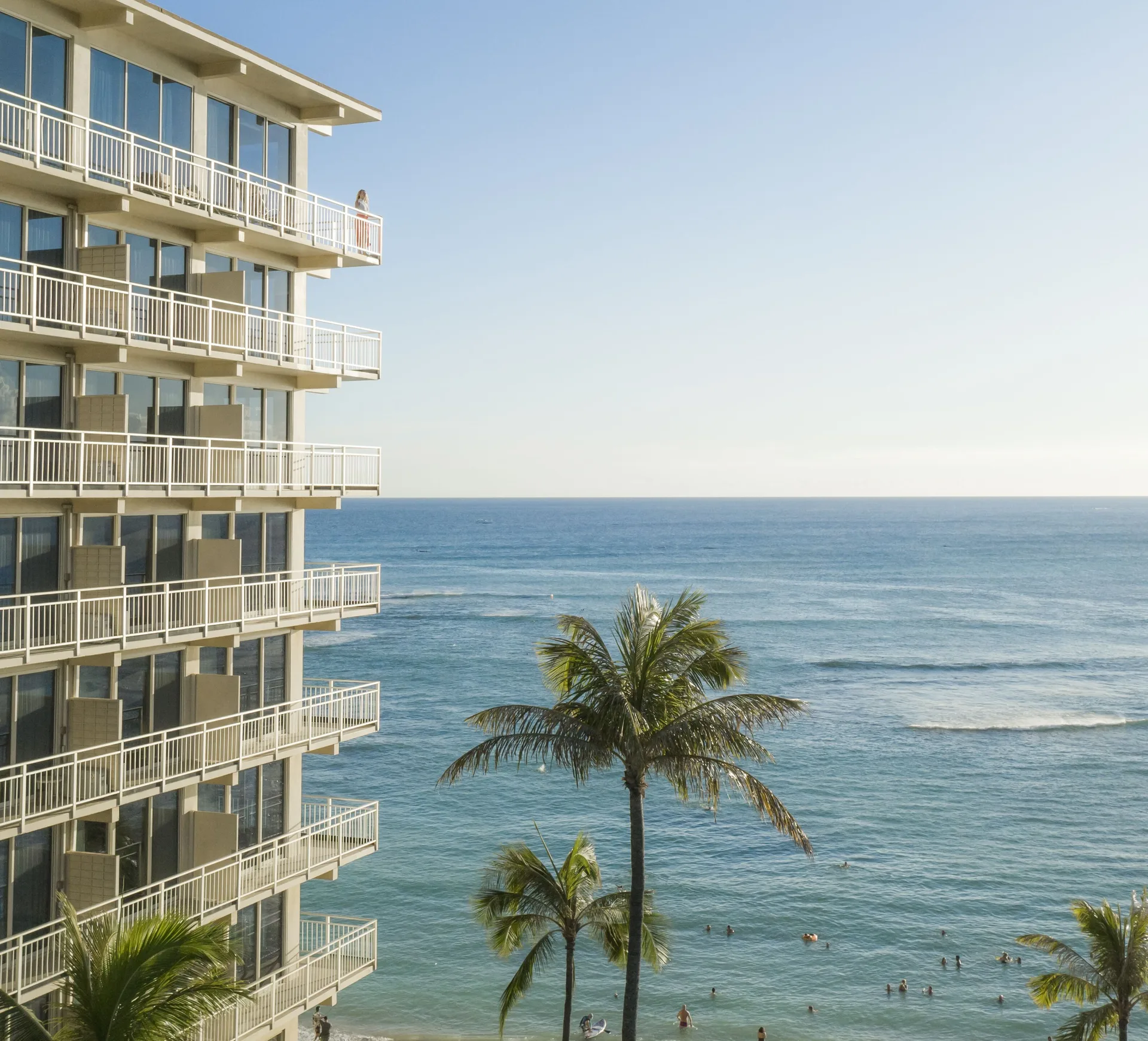 Balconies, palm trees, swimmers, and ocean water at Kaimana Beach Hotel.