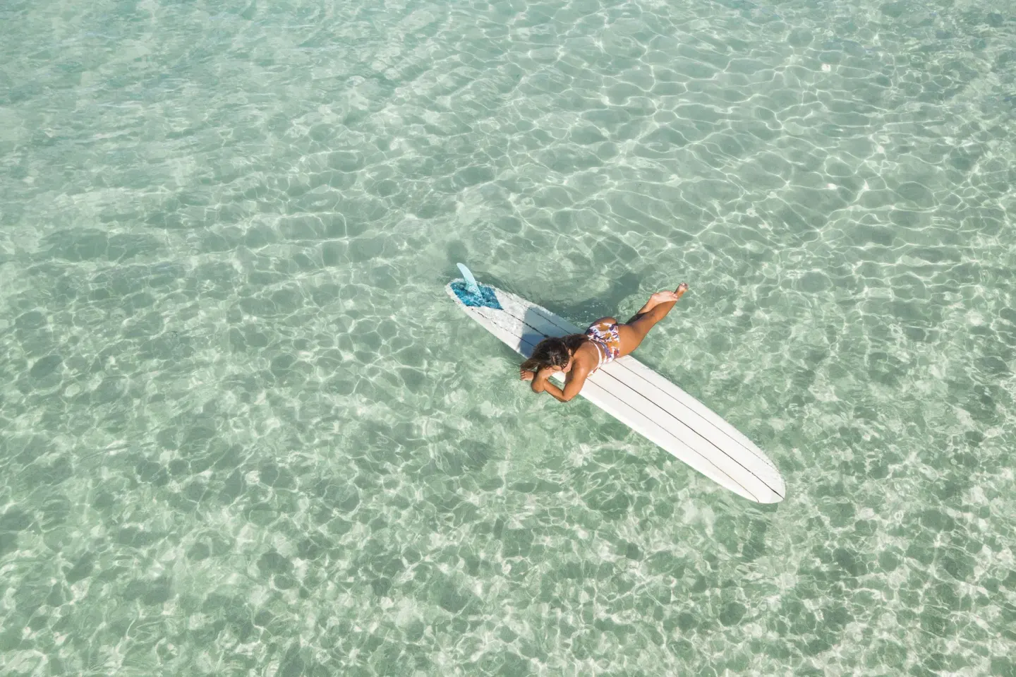 Person lying on a surfboard in clear shallow water at Kaimana Beach Hotel.