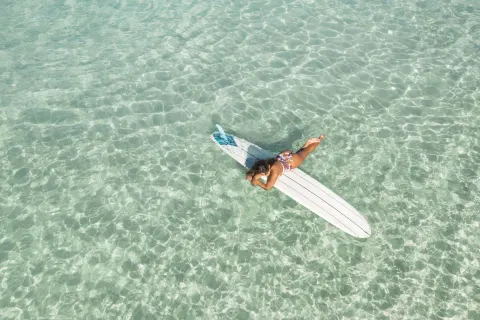 Person lying on a surfboard in clear shallow water at Kaimana Beach Hotel.