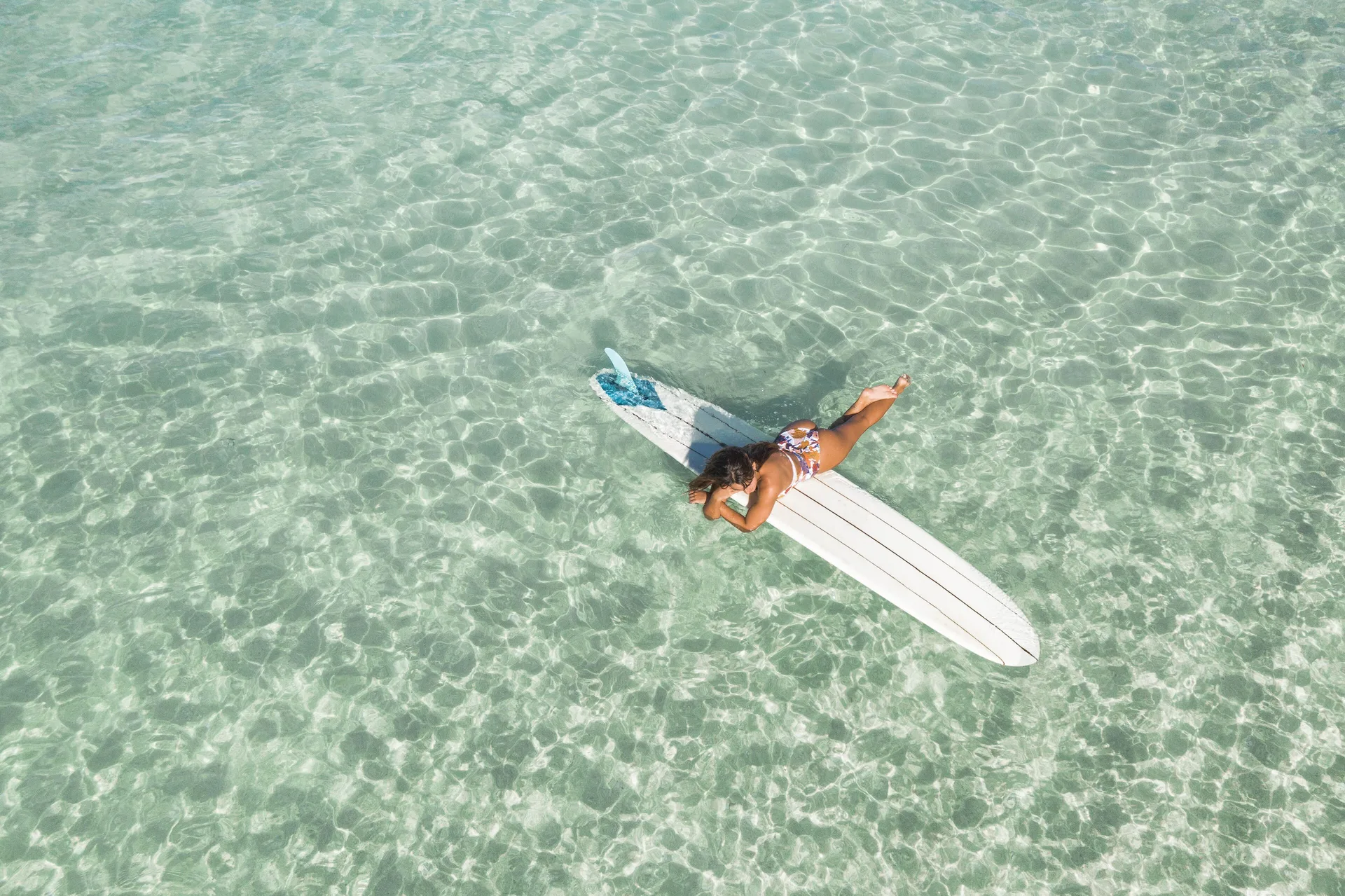 Person lying on a surfboard in clear shallow water at Kaimana Beach Hotel.