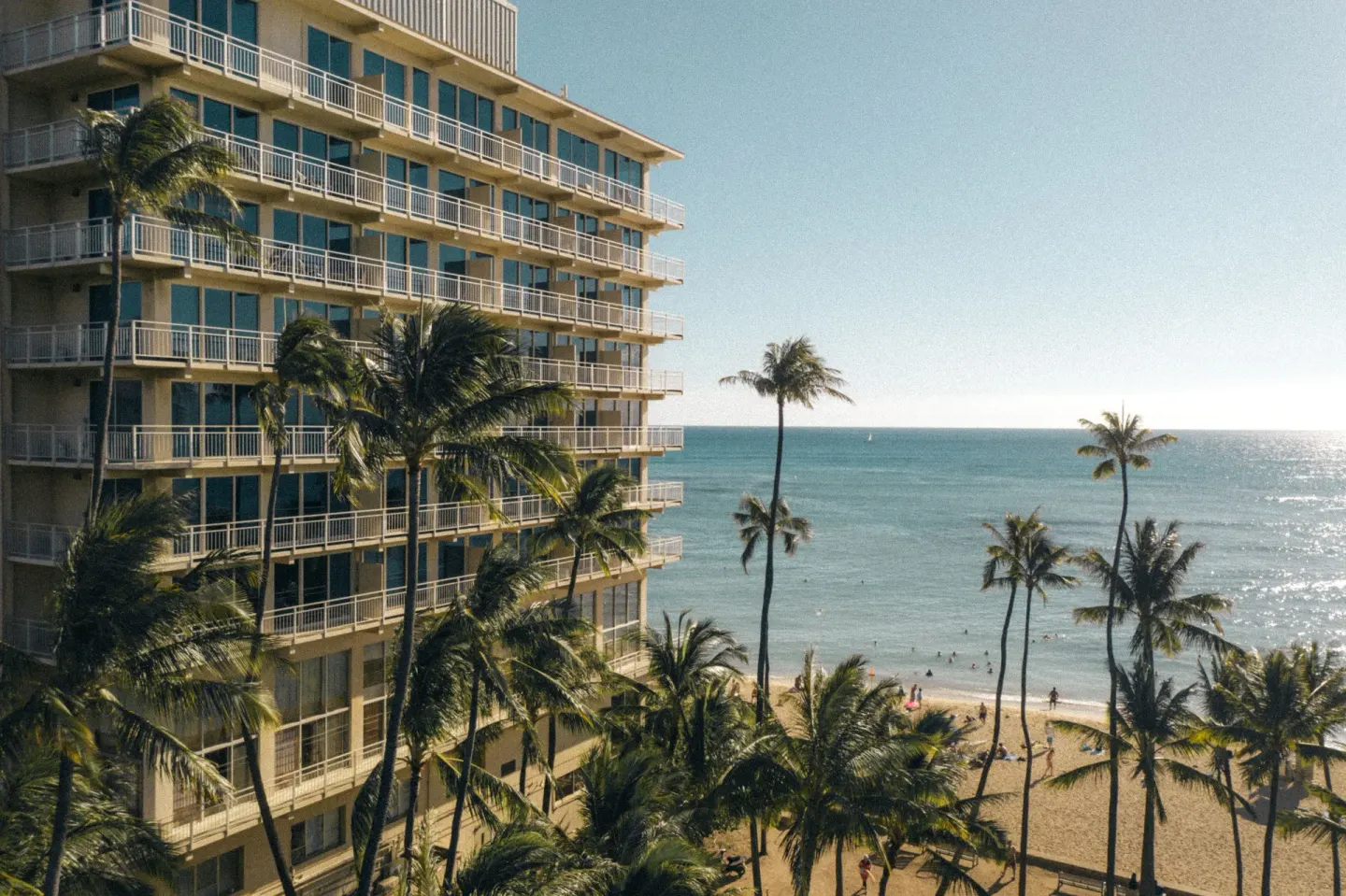 Hotel balconies, palm trees, beach, and ocean at Kaimana Beach Hotel.