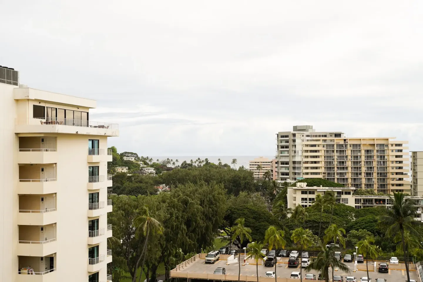 Classic Room balcony view of nearby buildings, palms, parking, and distant ocean at Kaimana Beach Hotel.