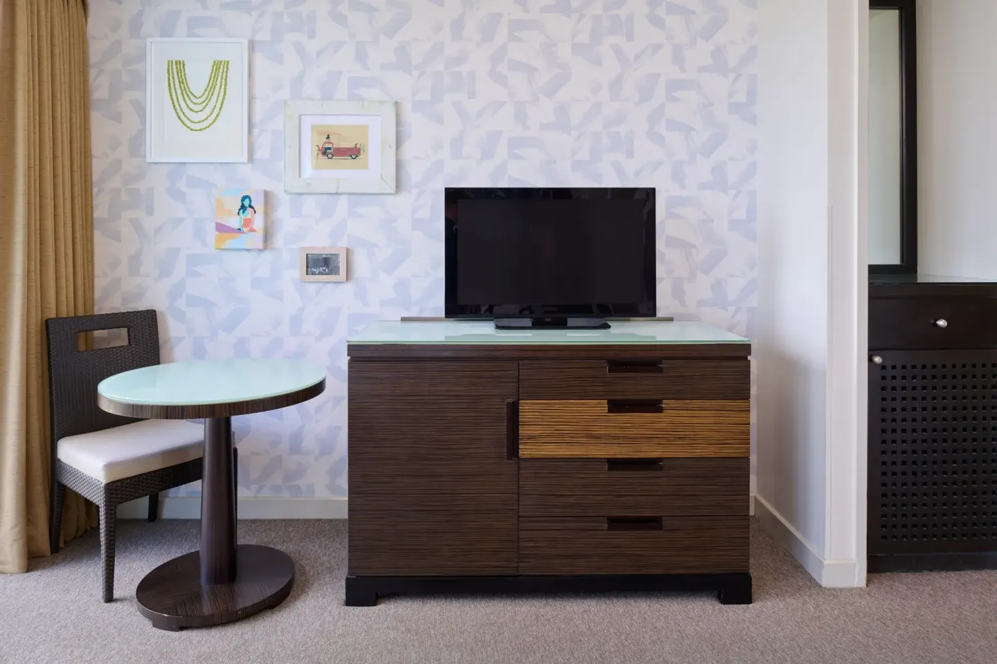 Classic Room dresser, TV, round table, and chair beside patterned wall art at Kaimana Beach Hotel.