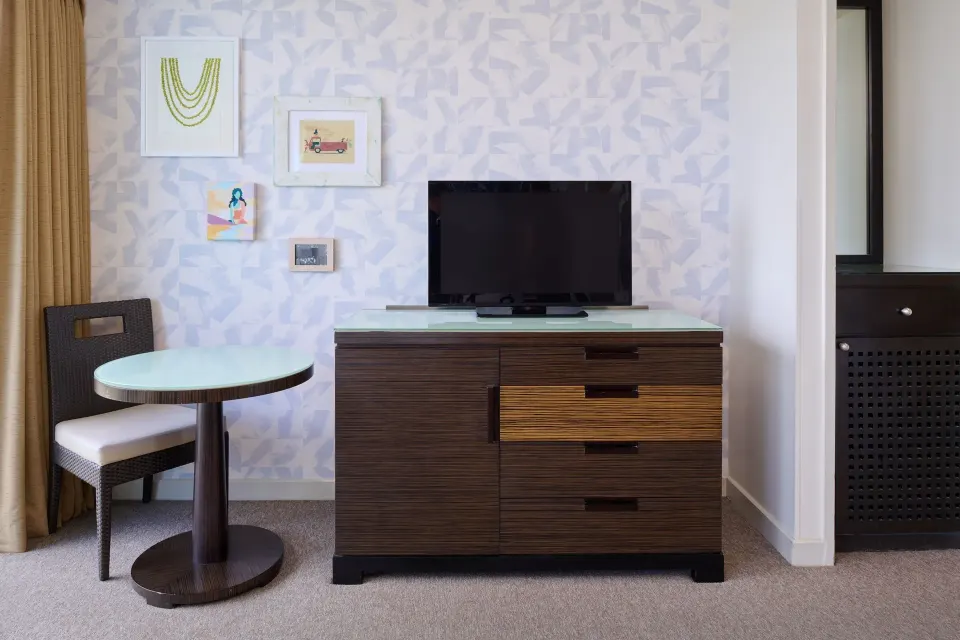 Classic Room dresser, TV, round table, and chair beside patterned wall art at Kaimana Beach Hotel.