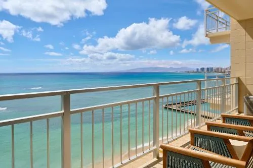 Oceanfront balcony with railing, chairs, and coastline view at Kaimana Beach Hotel.