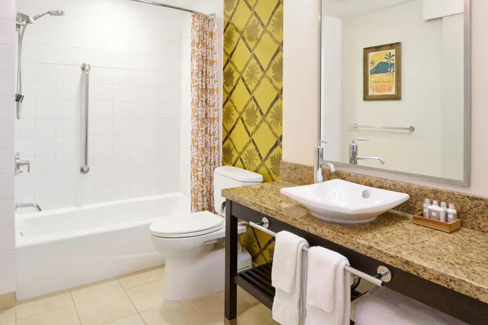 Ocean View room bathroom with tub, toilet, sink, and yellow accent wall at Kaimana Beach Hotel.