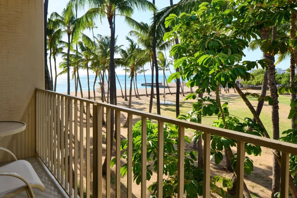 Park View room balcony with palms, lawn, and ocean beyond at Kaimana Beach Hotel.