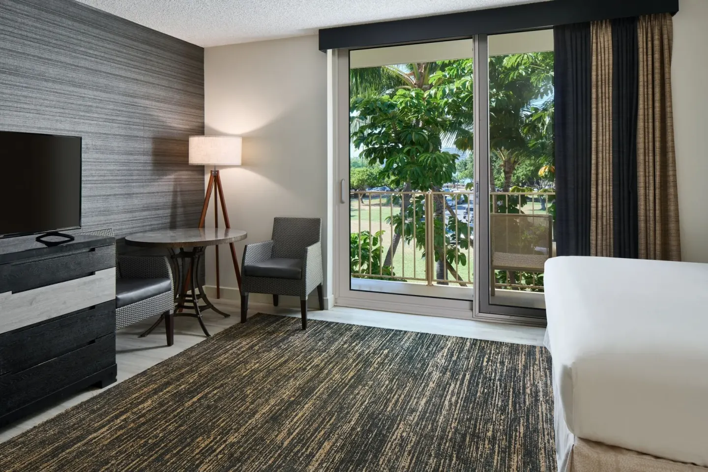 Park View room seating area, TV, and balcony doors at Kaimana Beach Hotel.