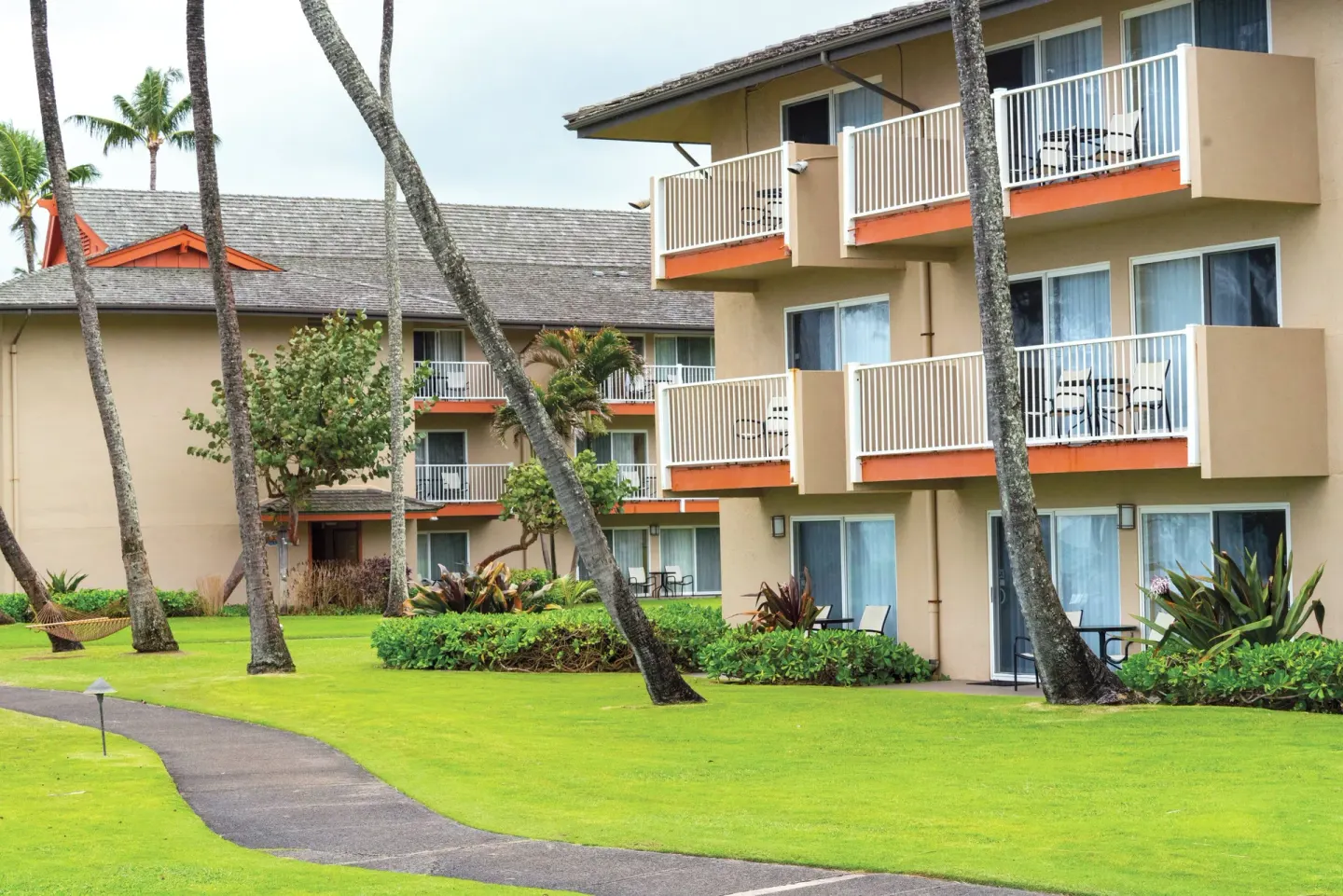 Guest buildings with balconies, palms, lawn, and walkway at Kauai Coast at the Beachboy.