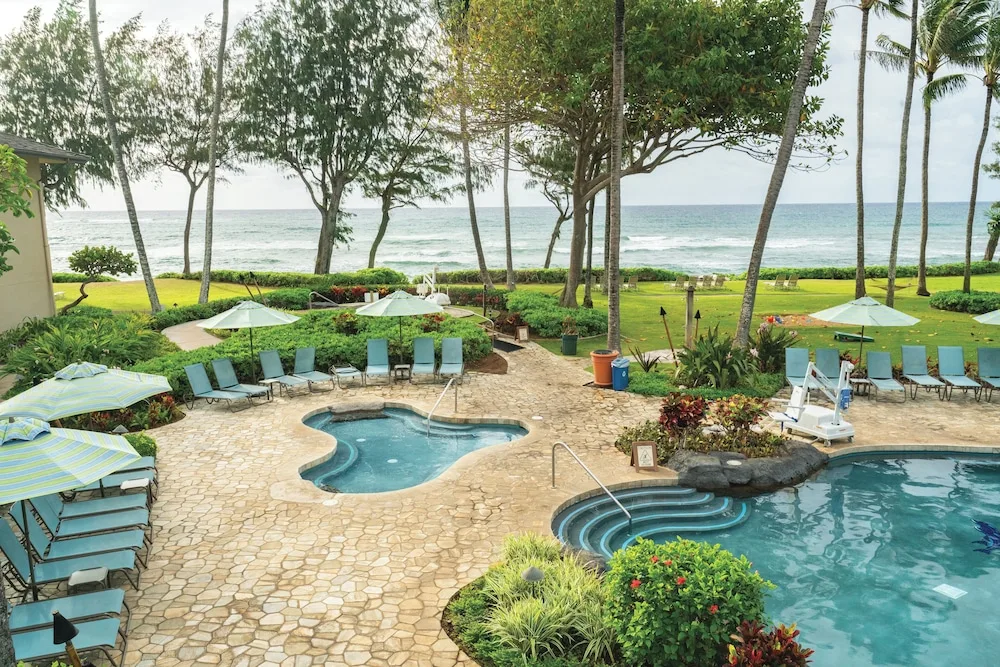 Oceanfront pool deck with lounge chairs and umbrellas at Kauai Coast at the Beachboy.