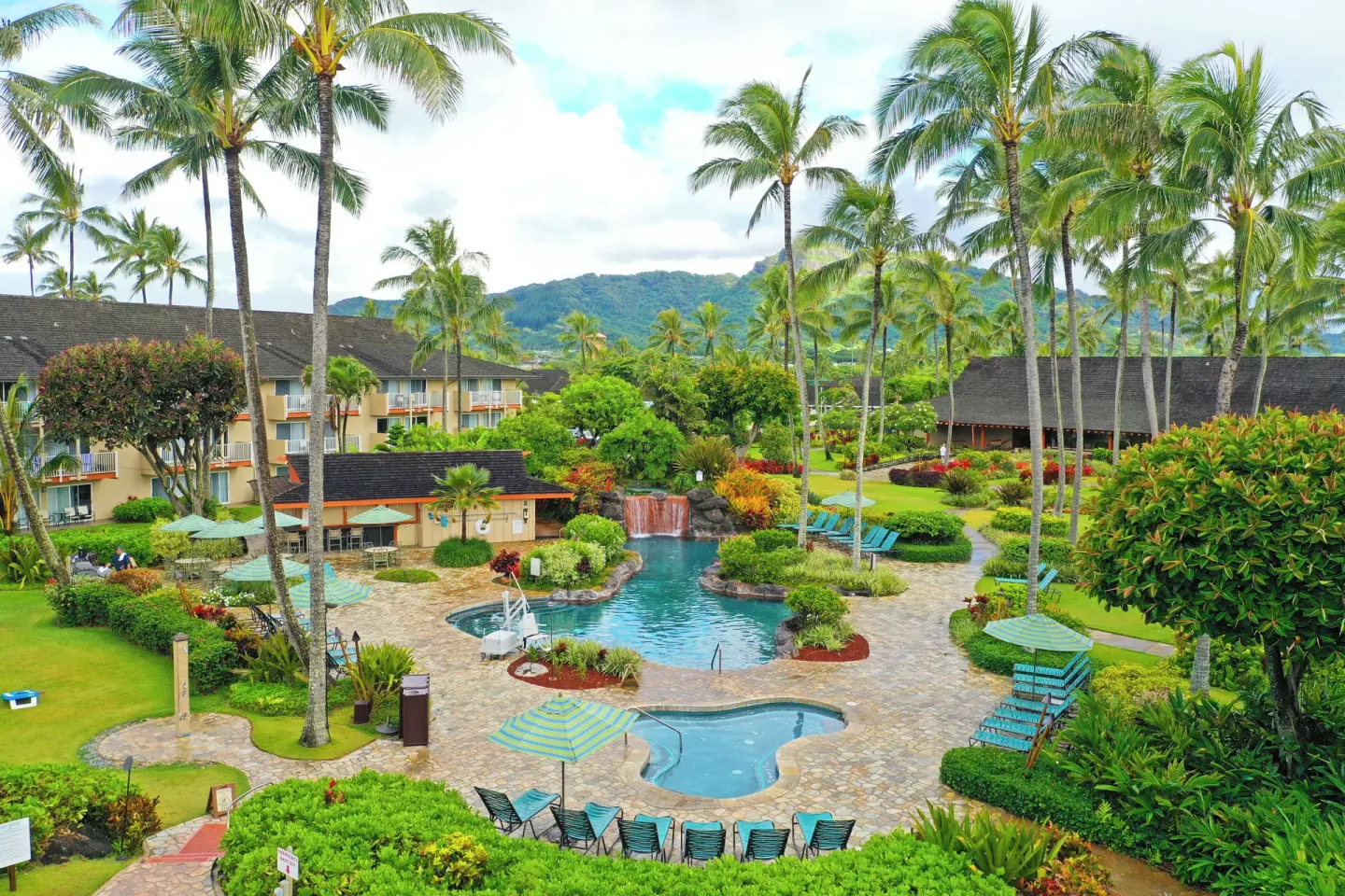 Resort pool area with waterfall, hot tub, palms, lounge chairs, and gardens at Kauai Coast at the Beachboy.