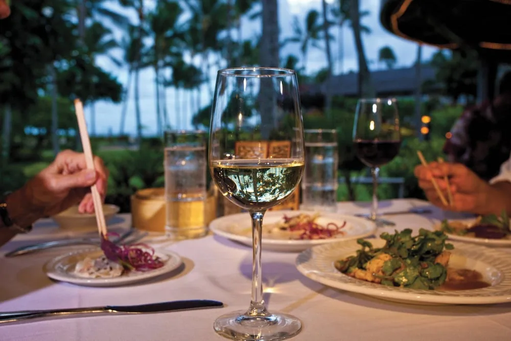 Wine glass and plated dishes on an open-air dining table at Kauai Coast at the Beachboy.