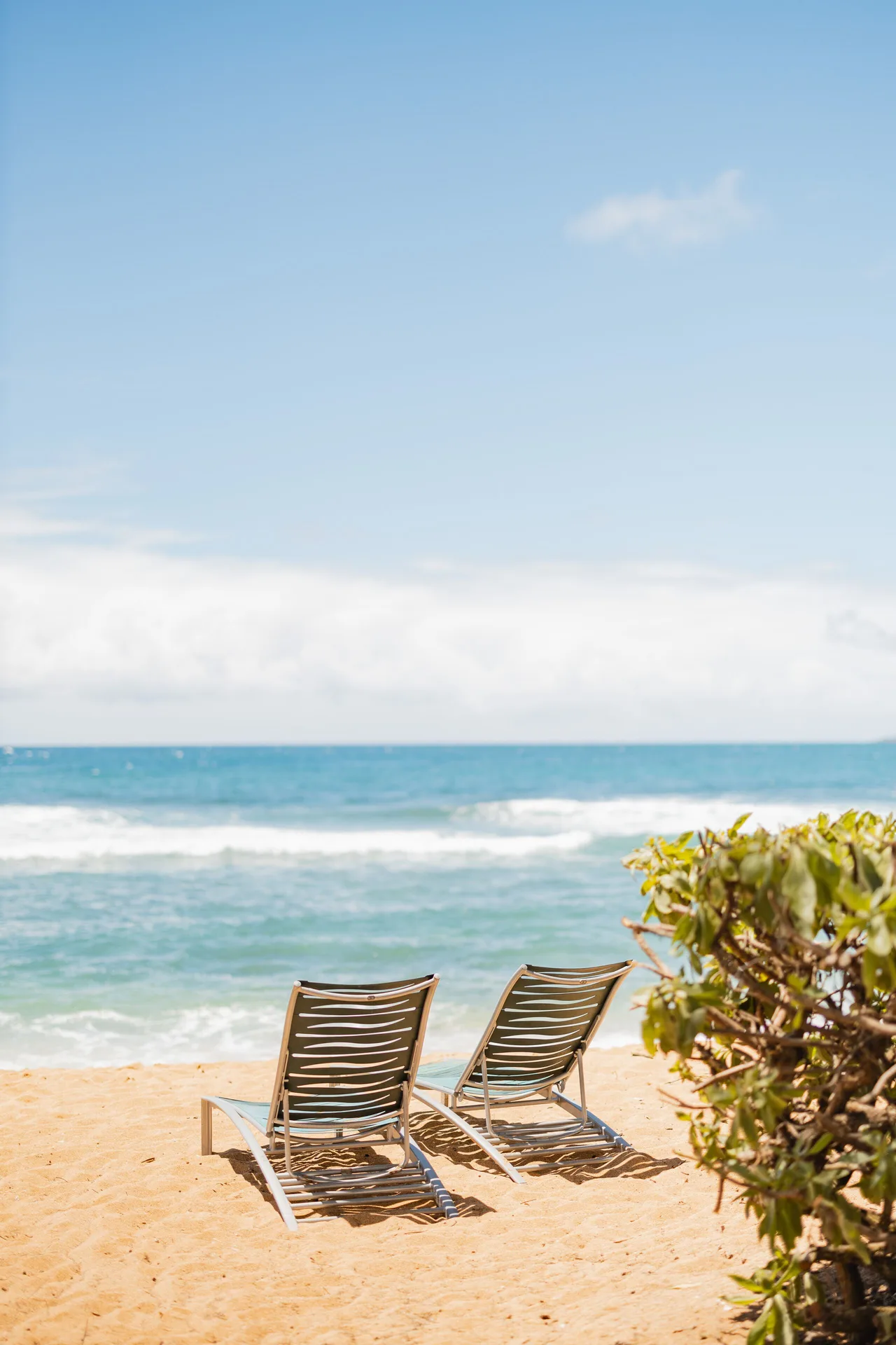 Two lounge chairs on the sandy beach by Kauai Shores Hotel.