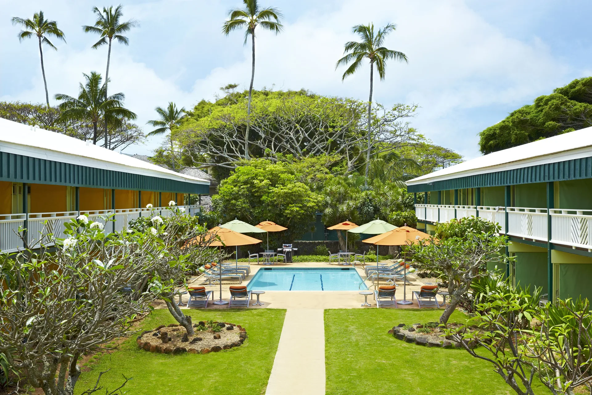 Courtyard pool with umbrellas, palms, lawns, and guest room buildings at Kauai Shores Hotel.