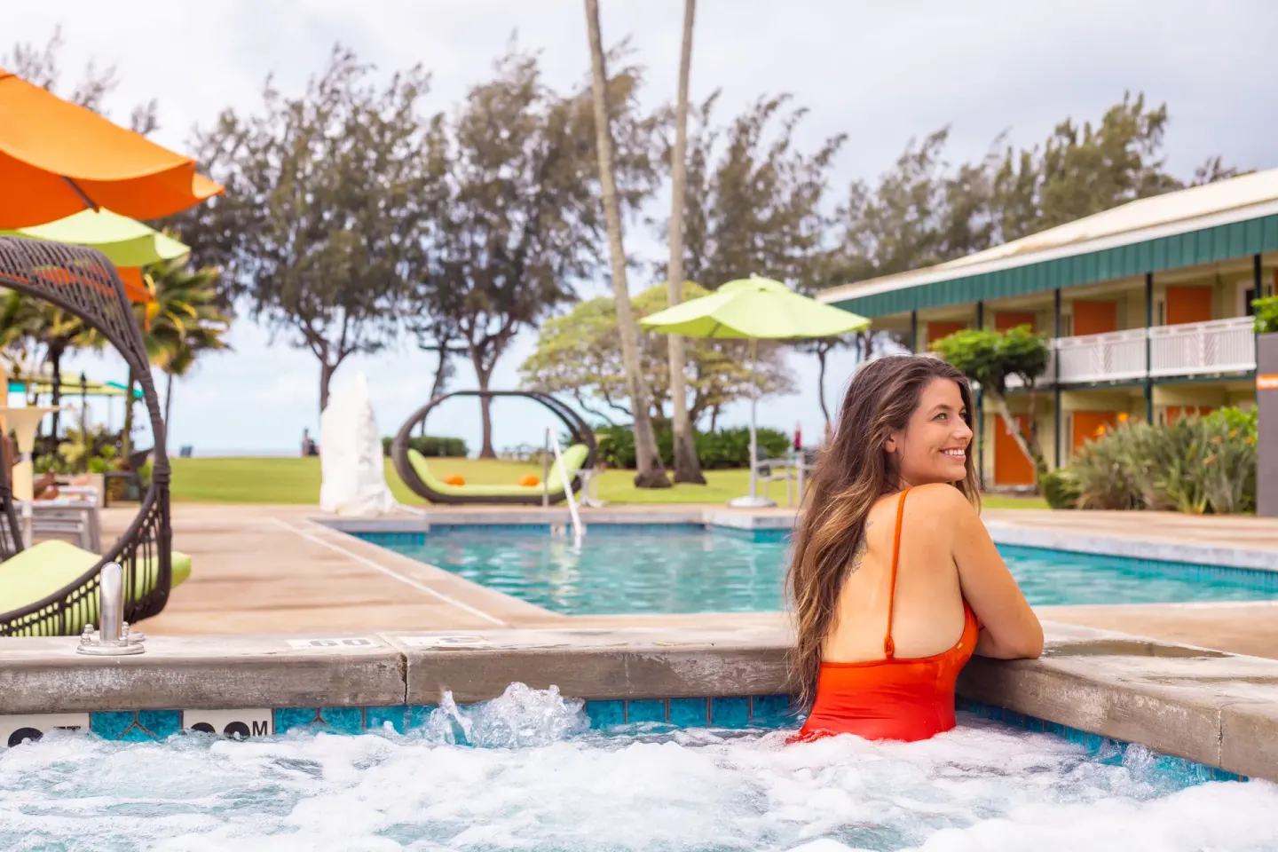 Guest in the hot tub at Kauai Shores Hotel with pool, umbrellas, and lawn beyond.