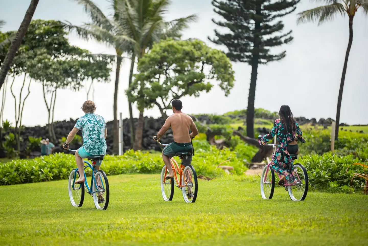 Guests ride cruiser bicycles across a green lawn at Kauai Shores Hotel.