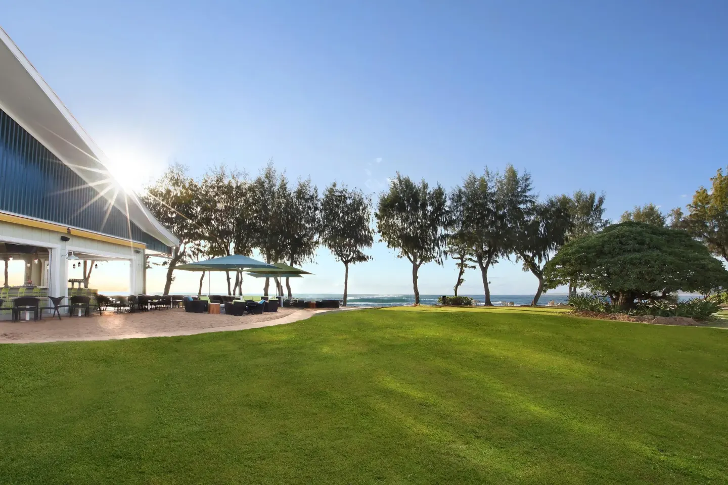 Sunny oceanfront lawn with patio seating and trees at Kauai Shores Hotel.