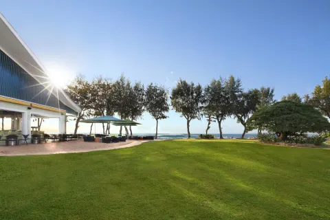 Sunny oceanfront lawn with patio seating and trees at Kauai Shores Hotel.