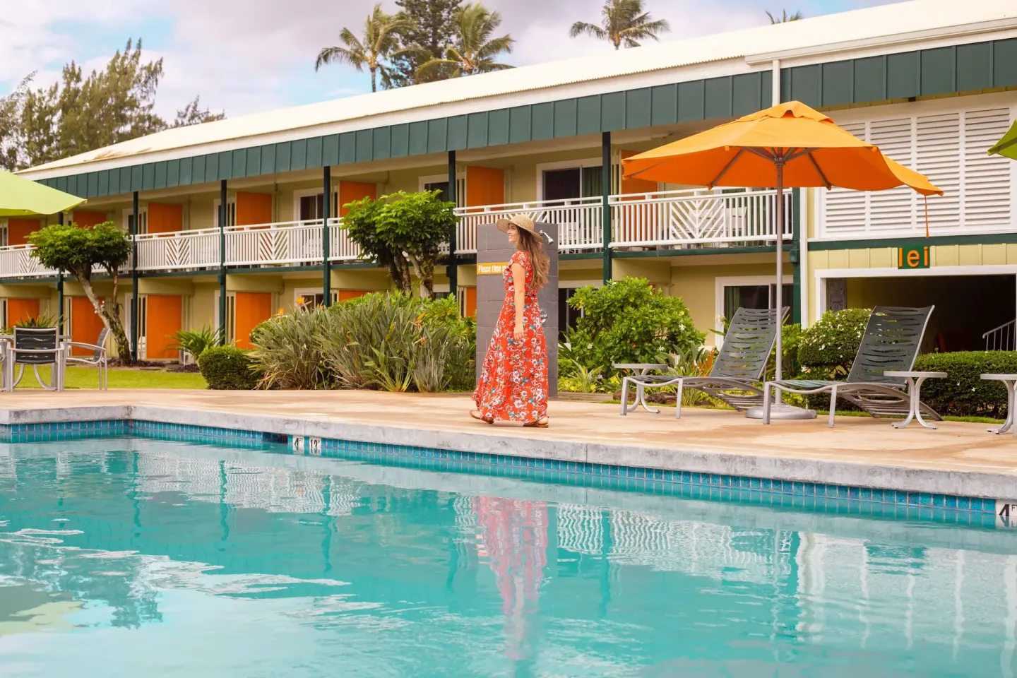 Pool deck at Kauai Shores Hotel with orange umbrellas, lounge chairs, and guest room balconies.