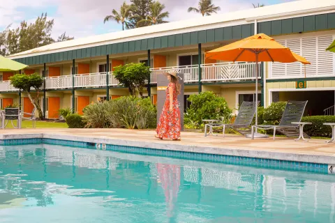 Pool deck at Kauai Shores Hotel with orange umbrellas, lounge chairs, and guest room balconies.