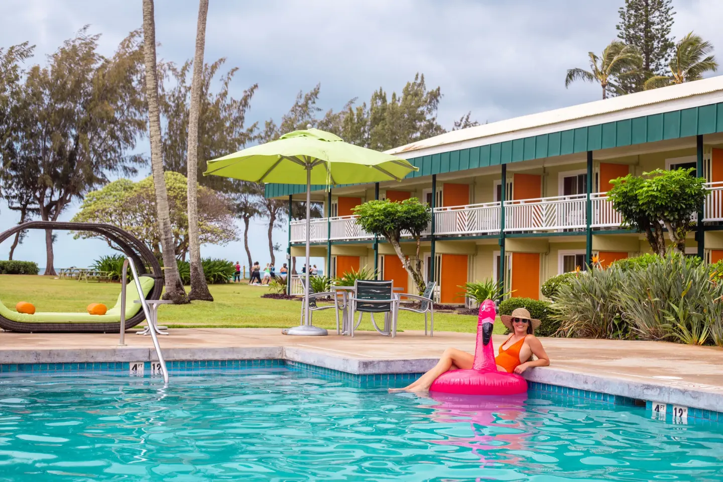 Guest floating in the pool at Kauai Shores Hotel with room balconies and lawn behind.