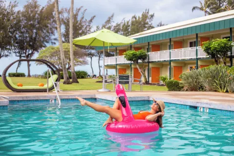 Guest relaxing on a pink flamingo float in the pool at Kauai Shores Hotel.