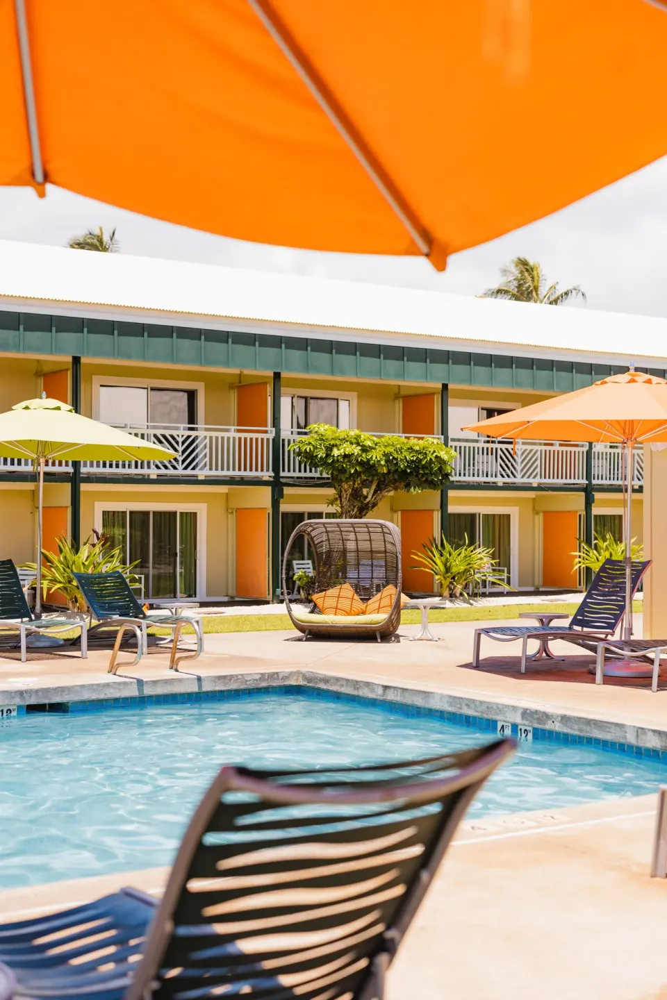 Pool with lounge chairs and orange umbrellas at Kauai Shores Hotel.