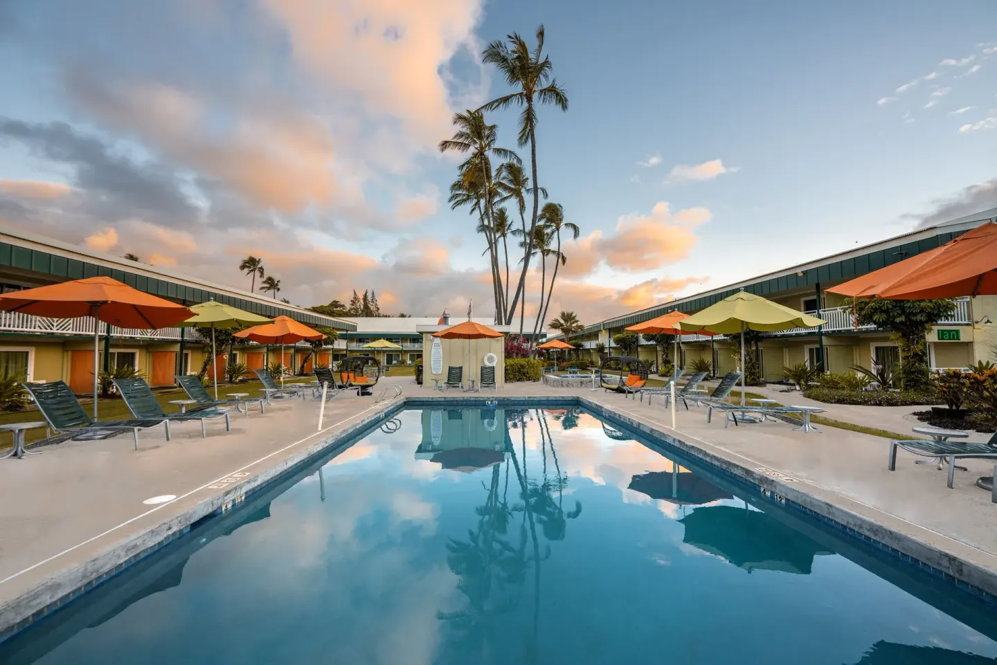 Reflective pool at Kauai Shores Hotel at sunset with lounge chairs, umbrellas, and palms.