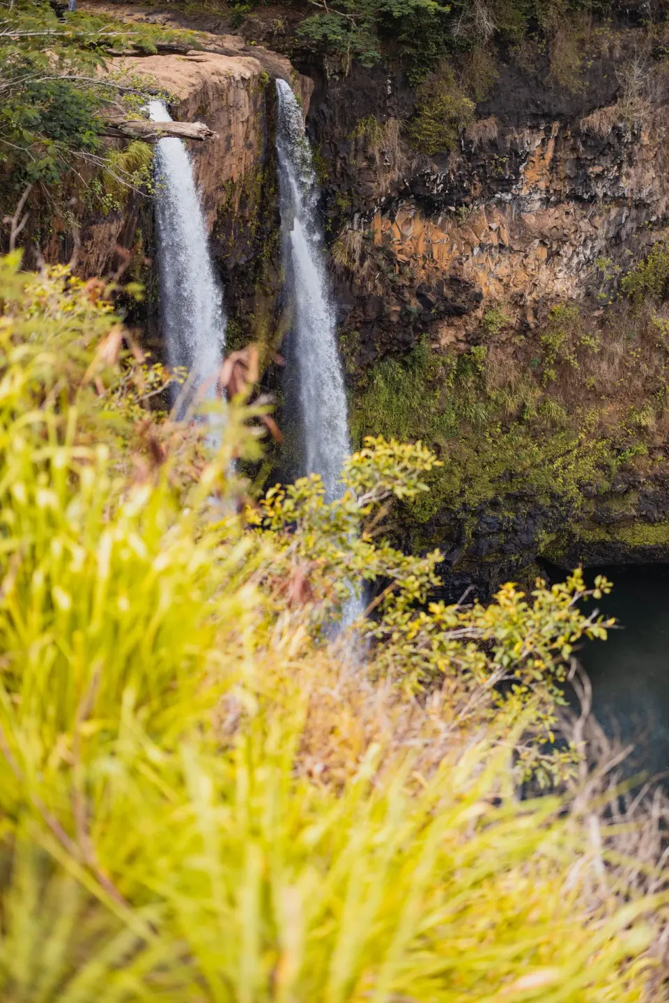A twin waterfall drops into a rocky basin near Kauai Shores Hotel.