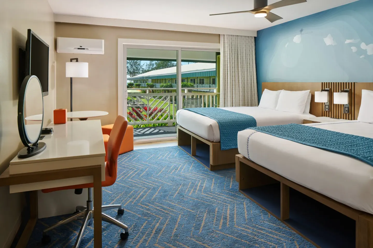 Ocean View room at Kauai Shores Hotel with two beds, desk, blue accent wall, and balcony.