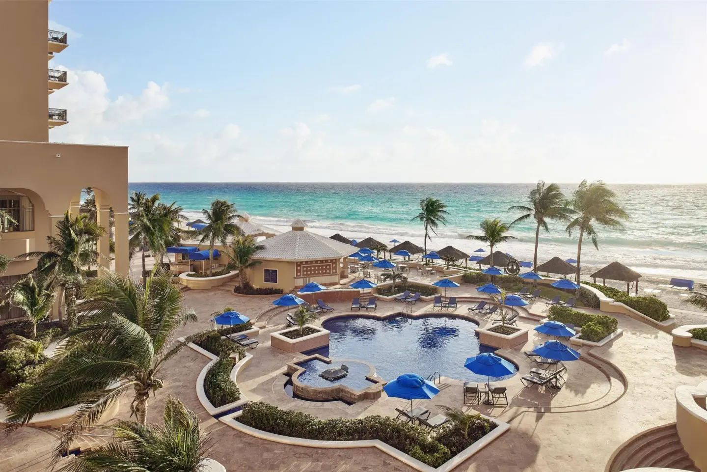 Beachfront pool area with palms and blue umbrellas at Kempinski Hotel Cancún.