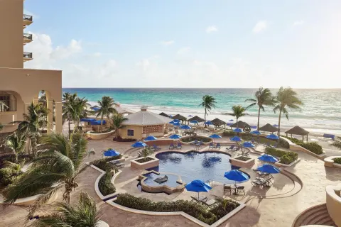 Beachfront pool area with palms and blue umbrellas at Kempinski Hotel Cancún.