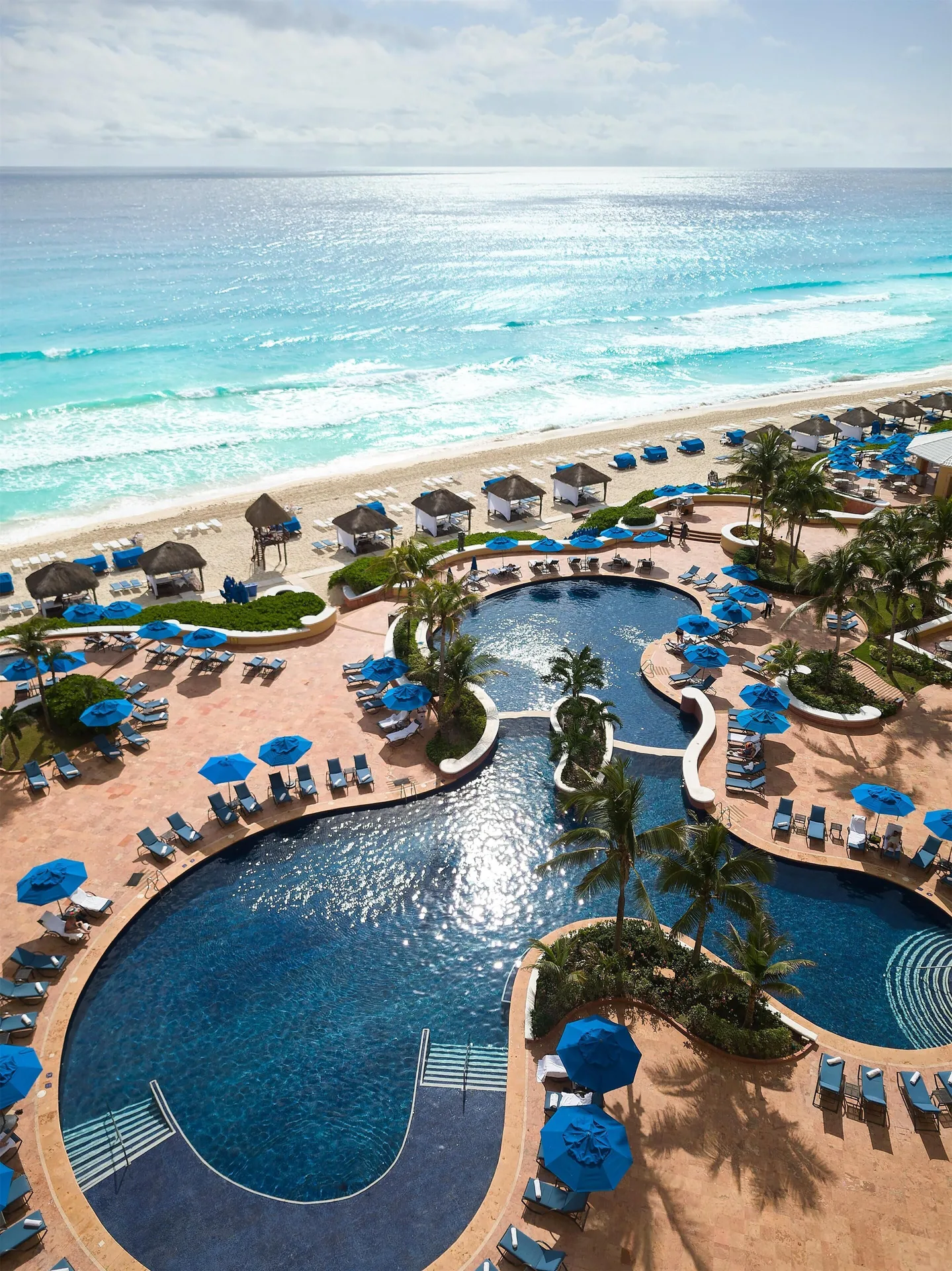 Beachfront pools, blue umbrellas and the Caribbean Sea at Kempinski Hotel Cancún.