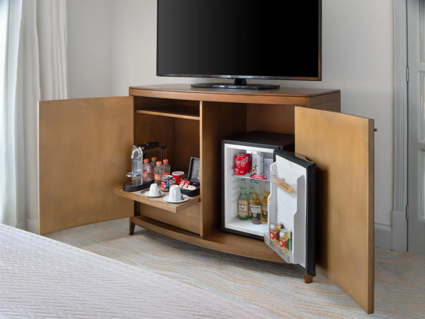 Guest room minibar cabinet with TV and open refrigerator at Kempinski Hotel Cancún.