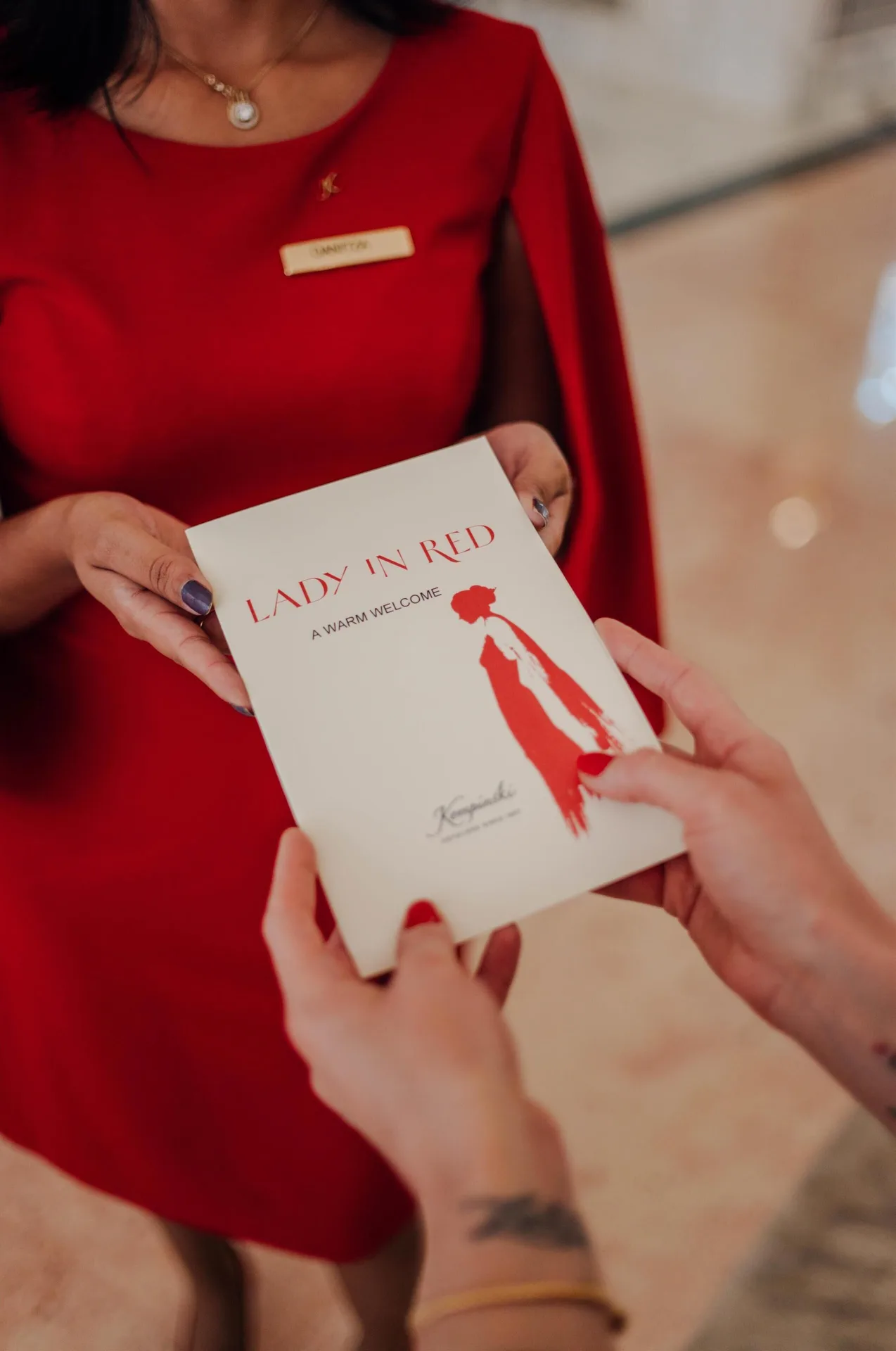Staff member in red hands a Lady in Red welcome card at Kempinski Hotel Cancún.