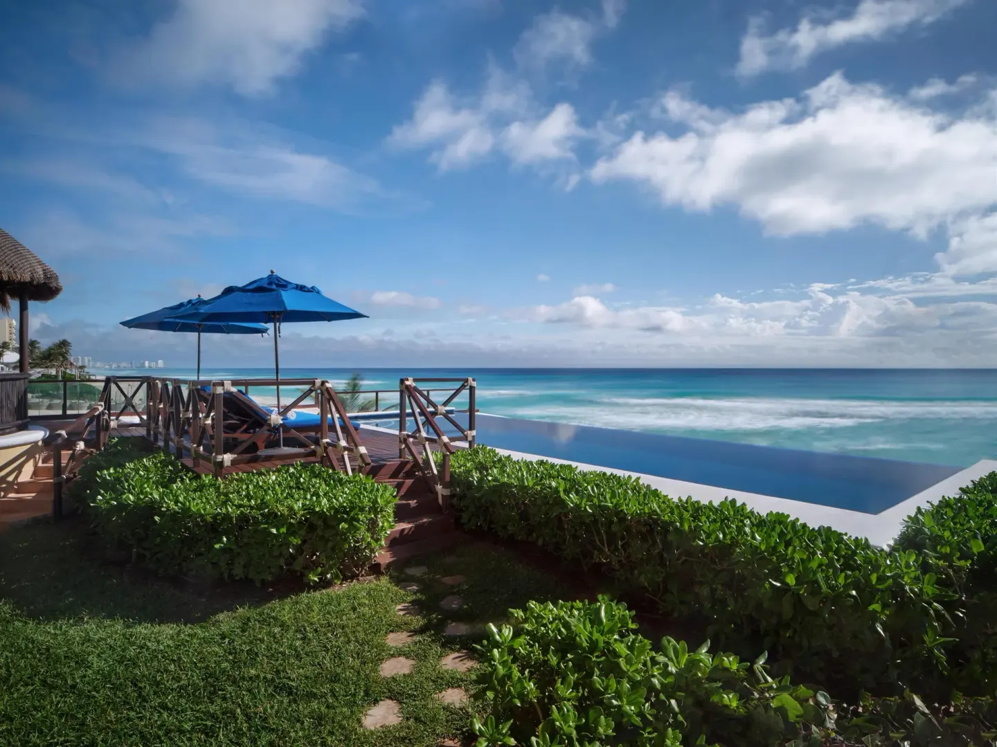 Oceanfront deck with blue umbrella and infinity pool at Kempinski Hotel Cancún.