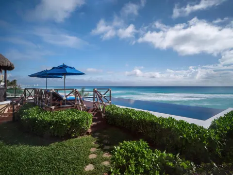 Oceanfront deck with blue umbrella and infinity pool at Kempinski Hotel Cancún.