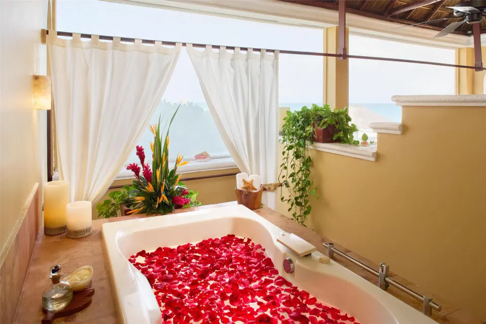 Petal-filled bathtub beside white curtains and ocean view at Kempinski Hotel Cancún.
