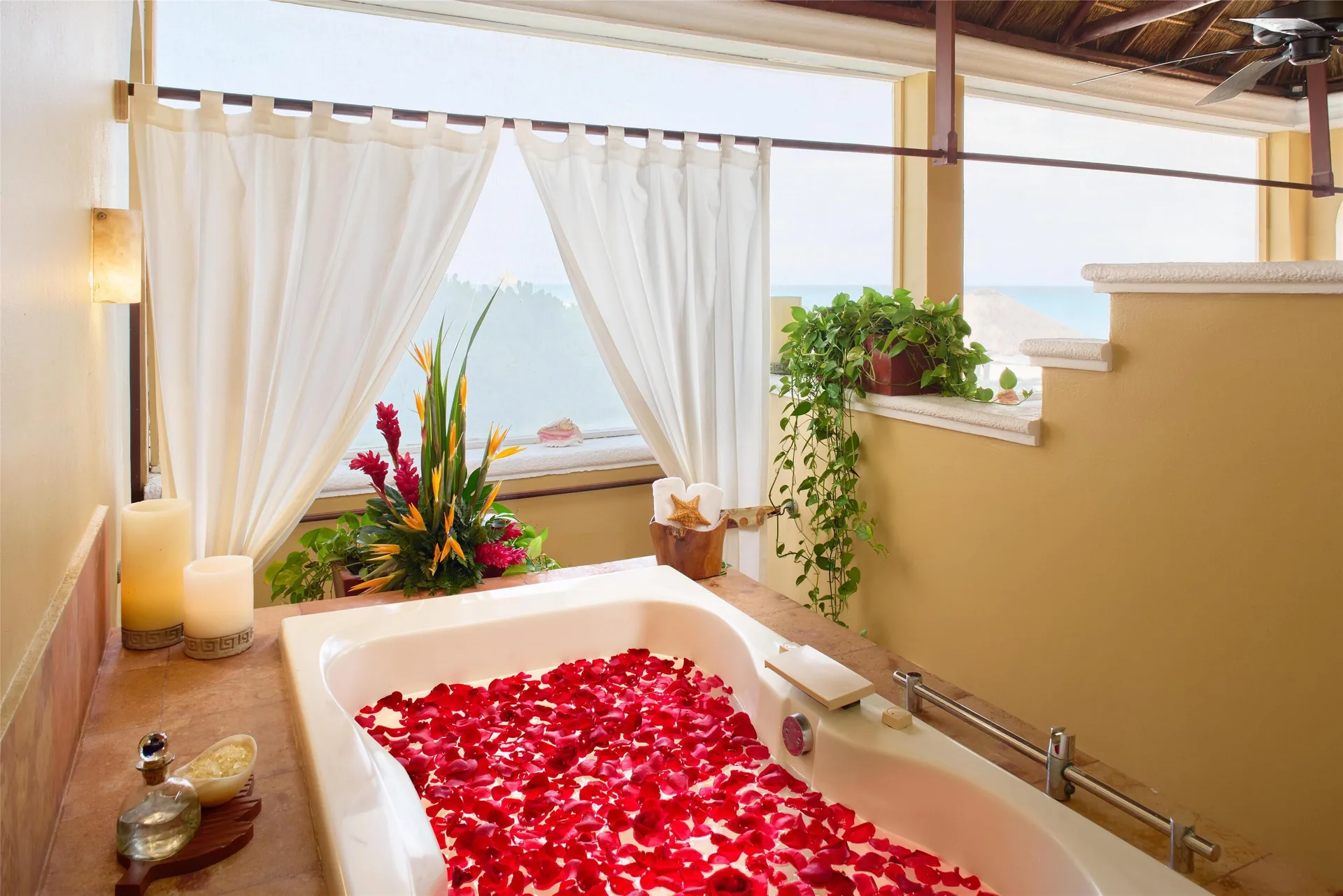 Petal-filled bathtub beside white curtains and ocean view at Kempinski Hotel Cancún.