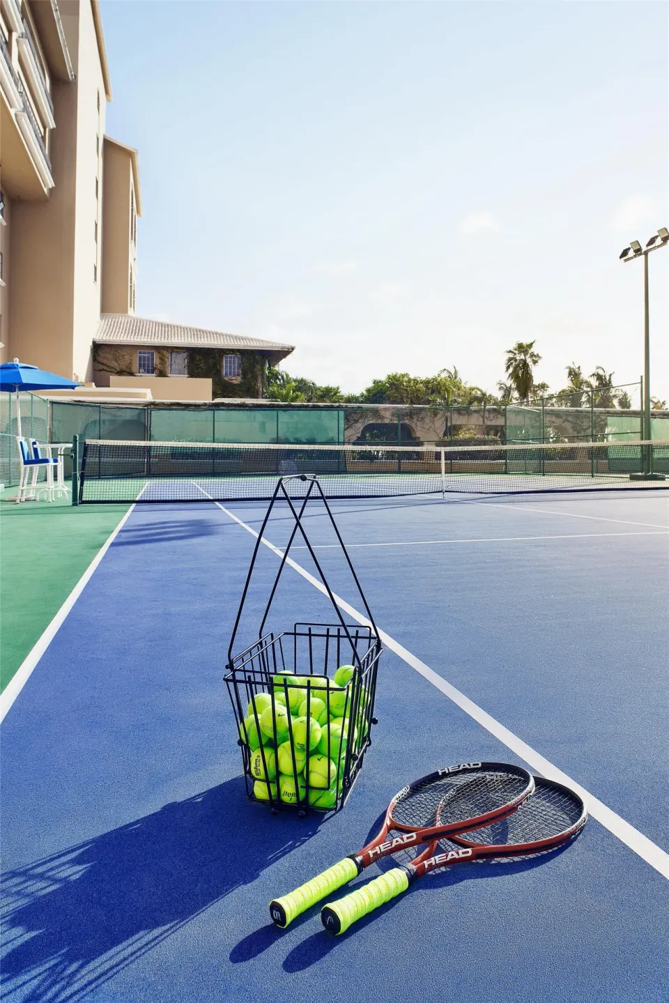 Tennis racquets and a basket of balls sit on a court at Kempinski Hotel Cancún.