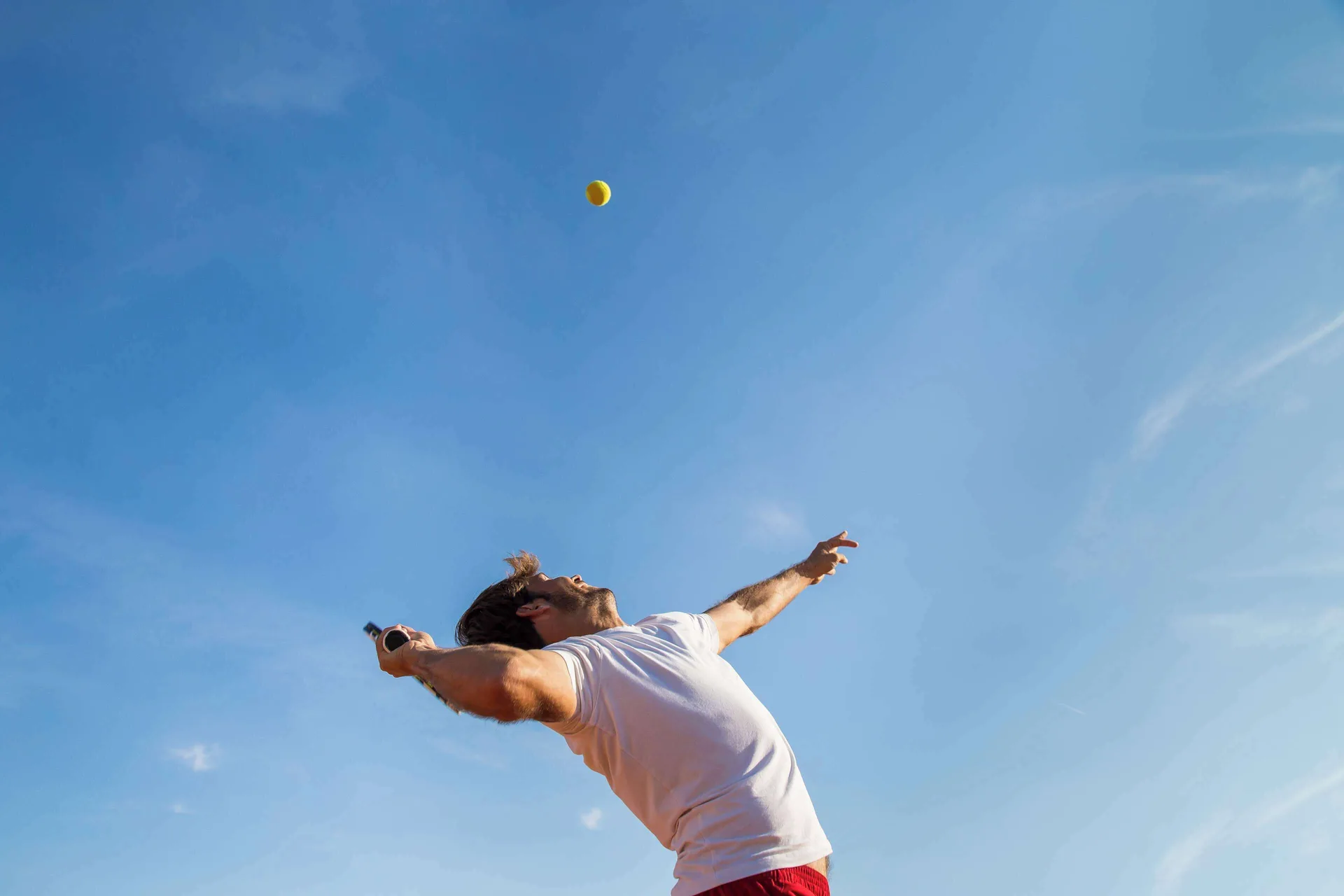 A tennis player serves against a clear blue sky at Kempinski Hotel Cancún.