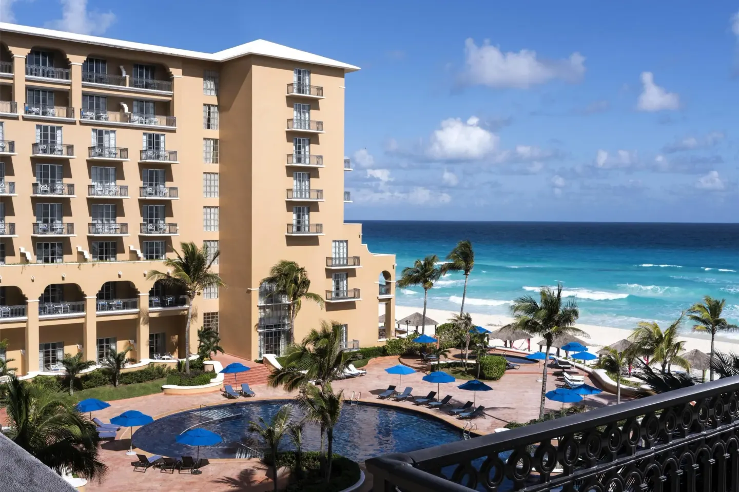 Balcony view of pool, palms, beach, and ocean at Kempinski Hotel Cancún.