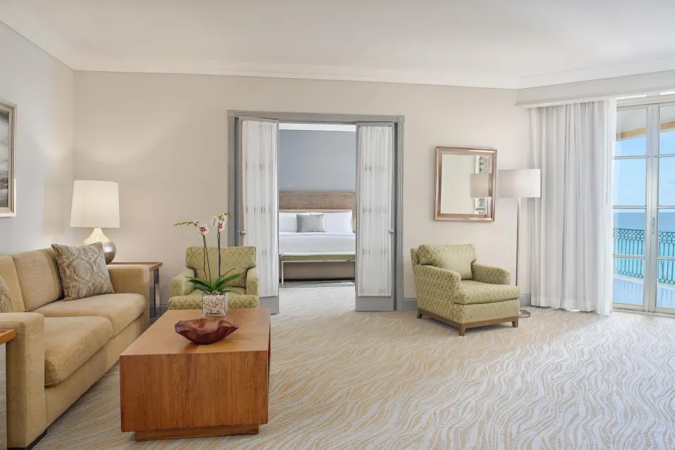 Seaside suite sitting room with sofa, armchairs and bedroom beyond at Kempinski Hotel Cancún.