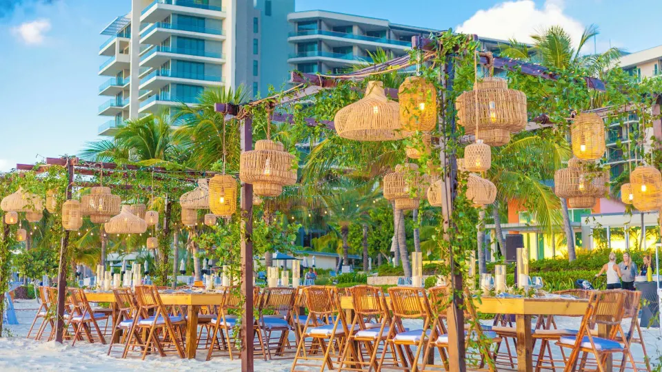 Wooden tables and woven lanterns on the sand near the resort at Kimpton Seafire Resort + Spa