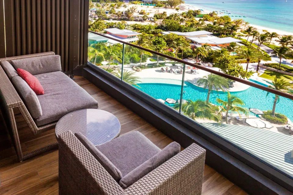 Balcony chaise and chair beside glass railing overlooking pool at Kimpton Seafire Resort + Spa