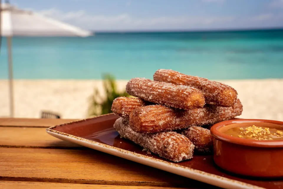 Plate of churros with dipping sauce and turquoise ocean in background at Kimpton Seafire Resort + Spa.